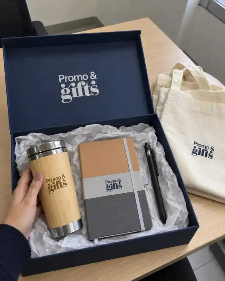Caja de regalo corporativo azul marino con termo de bambú, libreta y bolígrafo con logotipo, junto a una bolsa de tela