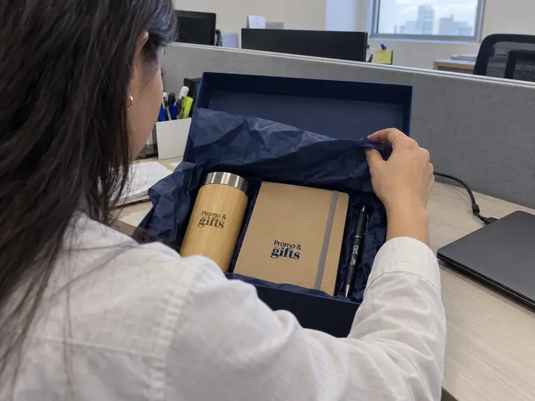 Colaboradora abre en su escritorio un kit de bienvenida con termo de bambú, libreta y bolígrafo